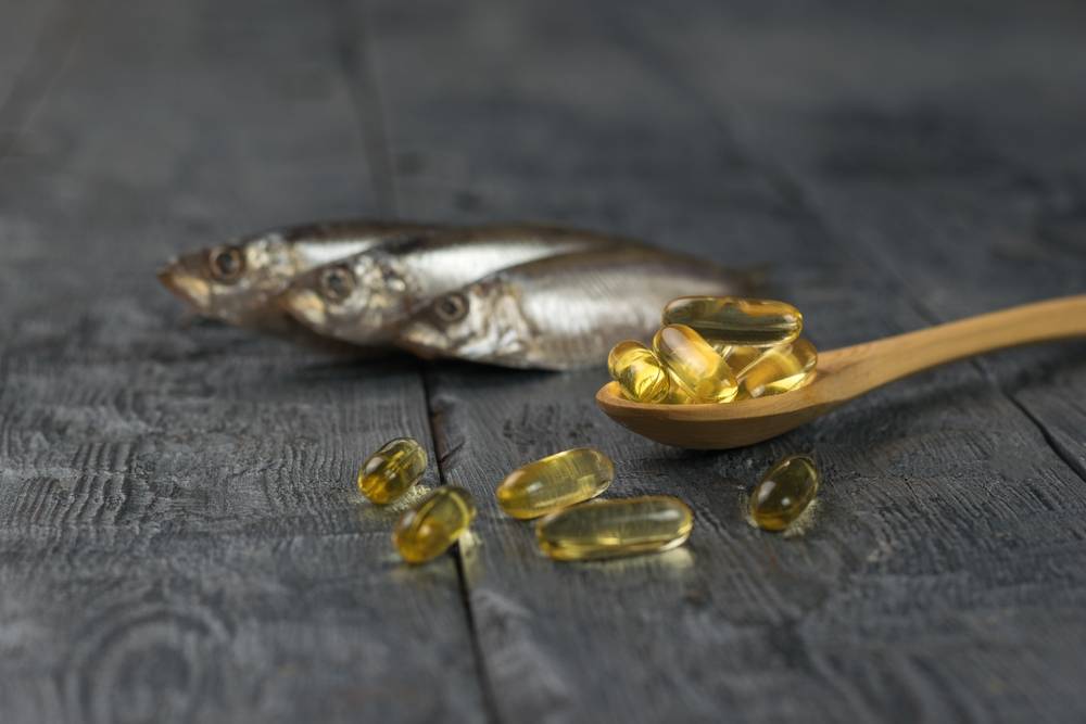 Wooden,Spoon,With,Fish,Oil,Capsules,On,The,Background,Of