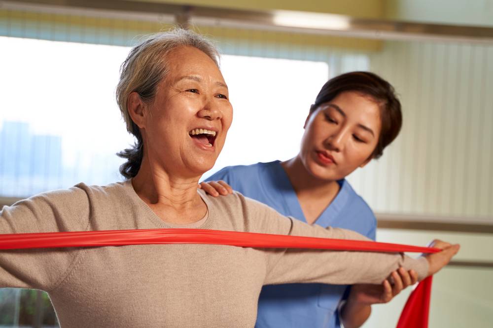 Happy,Senior,Asian,Woman,Exercising,Using,Resistance,Band,Guided,By