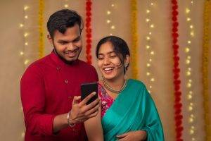 Indian,Couple,Using,Mobile,Phone,While,Celebrating,Diwali,At,Home